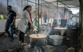 A woman stirs the contents of a large metal pot. 